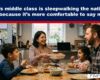 A smiling family of four sits around a kitchen table sharing a meal, with plates of pasta and glasses of water.