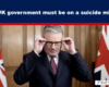 Man in a suit adjusts his glasses in front of British flags, beneath a bold banner that reads: 'The UK government must be on a suicide mission'.