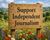 A wooden sign with "Support Independent Journalism" written on it, in a field of spring flowers