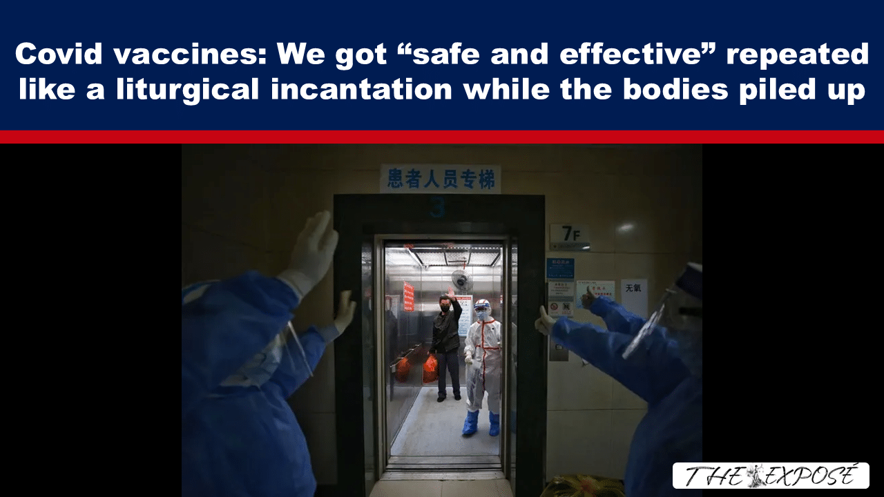 Medical staff in full PPE stand in an elevator corridor, guiding a patient into the elevator.